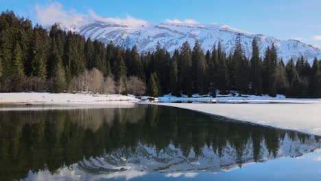 Reflection-of-Swiss-alps-in-a-calm,-half-frozen-lake-Lac-des-Mines-d'Or