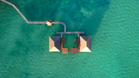 Top-down-view-of-a-water-bungalow-with-wooden-bridges-surrounded-by-beautiful-turquoise-water,-drone-flying-up-at-Leebong-Island-in-Belitung-Indonesia