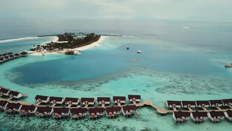 Drone-video-of-a-tropical-resort-in-the-Maldives,-blue-lagoon,-green-palms,-sunny-weather,-turquoise-shallow-water,-water-villas,-island-port,-4K