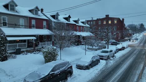 Snow-falling-on-quaint-city-street-with-houses-and-parked-cars-at-dusk