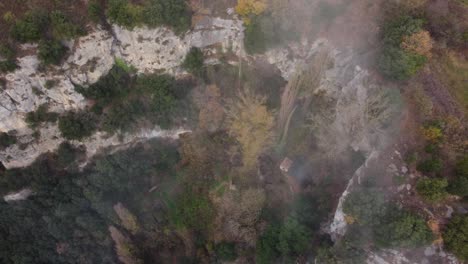 Misty-autumn-forest-and-cliffs-in-osona,-barcelona,-showing-a-lone-cabin,-aerial-view