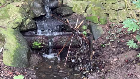 Un-Shishi-odoshi-En-Un-Jardín-Japonés-Con-El-Sonido-De-Un-Balancín-De-Bambú-Golpeando-Una-Roca-Que-Muestra-El-Flujo-De-Agua.