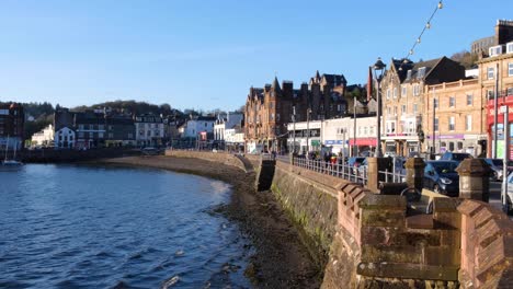 Vista-Panorámica-Escocesa-De-La-Ciudad-De-Oban-Con-Gente-Caminando-Y-Tráfico-Conduciendo-A-Lo-Largo-De-La-Costa-En-Un-Día-Soleado-De-Cielo-Azul-En-El-Oeste-De-Escocia,-Reino-Unido