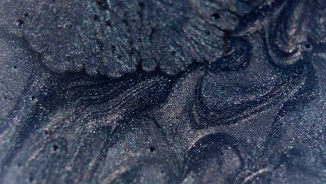Close-up-of-swirling-dark-blue-and-black-ink-patterns-in-water,-shimmering-with-specks-of-light