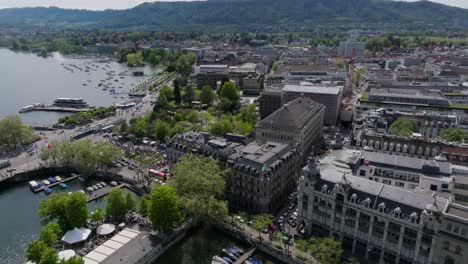 Left-moving-drone-footage-of-Zurich-city-skyline-and-lake-front-with-cars,-public-transport,-boats-and-people