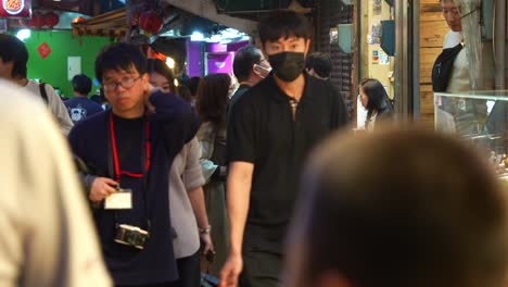 Tourists-wander-through-a-charming-alleyway-lined-with-food-stalls-and-gift-shops-within-Jiufen-Old-Street,-vendors-giving-out-samples,-a-popular-tourist-spot-nestled-in-Taiwan's-mountain-town