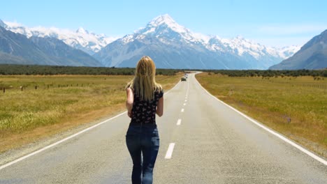 Girl-standing-by-renowned-State-Highway-80,-adjacent-to-Lake-Pukaki,-with-a-view-of-Mount-Cook