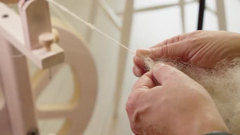 Close-up-hands-pull-natural-wool-fiber-as-it-feeds-into-spinning-wheel