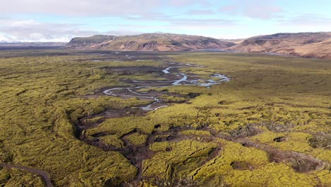 Meandering-river-through-vibrant-green-mossy-icelandic-landscape,-aerial-view