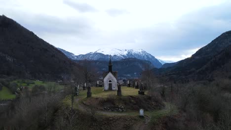 Mysterious-looking-shot-of-Chapelle-on-a-top-of-a-hill-surrounded-by-circle-of-gravestones-and-mountains