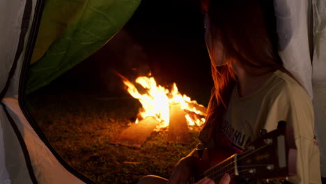 Cerca-De-Un-Joven-Viajero-Asiático-Tocando-Solo-La-Guitarra-Ukelele-Frente-A-Una-Hoguera-Por-La-Noche-Dentro-De-Su-Tienda-De-Campaña