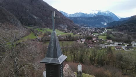 Kreuz-Der-Kirche-über-Dem-Tal-Mit-Sonnenaufgang-Und-Kleiner-Stadt-Im-Bergtal-Im-Hintergrund