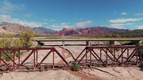 Drone-Volando-Sobre-Un-Puente-Ferroviario-Y-Un-Puente-Para-Automóviles-En-La-Ruta-9-En-Jujuy,-Argentina,-Con-Un-Impresionante-Telón-De-Fondo-De-Coloridas-Montañas