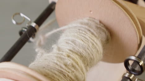 Closeup-spinning-wheel-bobbin-collects-spool-of-natural-grey-wool-yarn