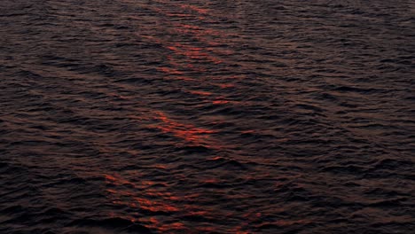 Beautiful-sunset-red-light-dances-on-wave-tops-of-ocean-water-surface,-aerial-dolly
