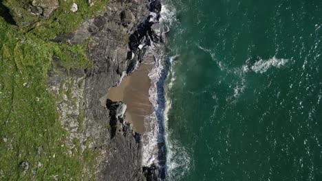 Cornish-Beach-Cove-with-Ocean-Waves-Crashing-Against-the-Rocks-from-a-Top-Down-Descending-Drone-Shot,-Cornwall,-UK