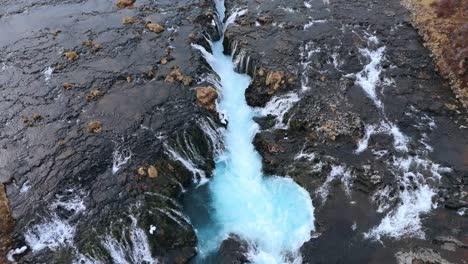 Der-Atemberaubende-Bruarfoss-Wasserfall-In-Island-Mit-Seinem-Leuchtend-Blauen-Wasser-Und-Seiner-Felsigen-Umgebung,-Luftaufnahme