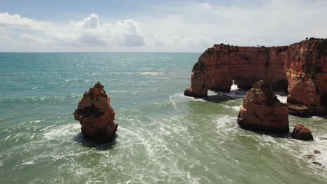 Two-natural-arches-with-sea-stacks-and-waves-crashing-aerial-4k-drone-reverse-pan-down-view-on-the-scenic-Estrada-da-Caramujeira-beach-in-the-Algarve-region-of-Portugal