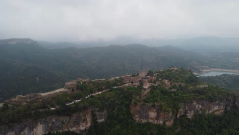 Siurana,-a-historic-village-atop-a-cliff-in-tarragona,-with-misty-mountains-in-the-background,-aerial-view