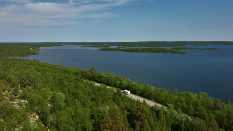 Vista-Aérea-Siguiendo-Una-Caravana-Conduciendo-Frente-Al-Lago-Inarinjarvi-En-Finlandia