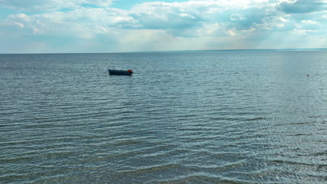 solitary-boat-floating-on-a-vast,-calm-sea-under-a-sky-with-light-streaming-through-clouds