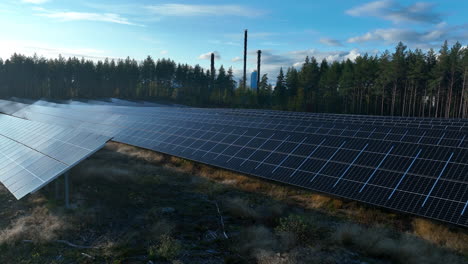 Drone-flying-over-a-sunlight-collector-field-with-forest-and-chimney-background