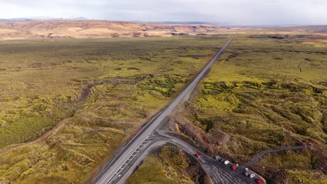 A-lone-road-winding-through-icelandic-mossy-landscape,-vehicles-in-motion,-aerial-view