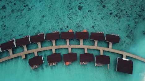 Drone-top-down-rotating-video-of-a-tropical-resort-in-the-Maldives,-blue-lagoon-reef,-sunny-weather,-turquoise-shallow-water,-water-villas,-island-wooden-road,-4K