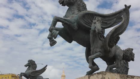 Statue-of-winged-horse-of-pegasus-at-docks-of-Cartagena-with-clock-tower-in-the-background,-Colombia