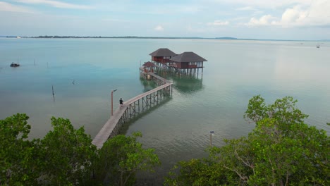 Static-Aerial-of-a-man-riding-a-bicycle-on-a-pier-towards-an-overwater-villa-in-the-middle-of-the-sea