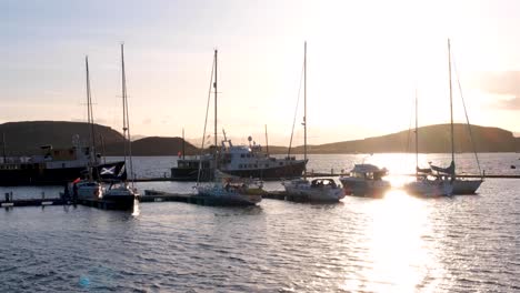 Shimmering-light-cast-over-ocean-water-during-sunset-with-moored-boats-and-ships-in-harbour-in-Oban-town,-Western-Scotland-UK