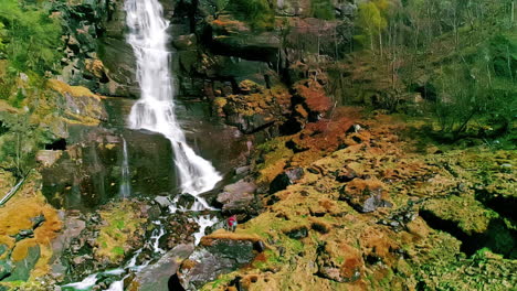 Drohnenaufnahme,-Die-Zurückfährt-Und-Einen-Großen-Wasserfall-In-Norwegen-Freigibt,-Unter-Dem-Zwei-Menschen-Stehen
