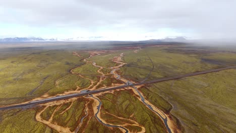 Toma-Aérea-De-Un-Vasto-Paisaje-Islandés-Con-Ríos-Trenzados-Y-Una-Carretera-Solitaria