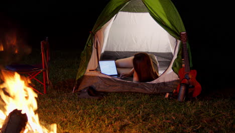 Digitale-Nomadin,-Junges-Mädchen,-Das-Nachts-Beim-Camping-Von-Ihrem-Zelt-Aus-Vor-Dem-Lagerfeuer-Arbeitet