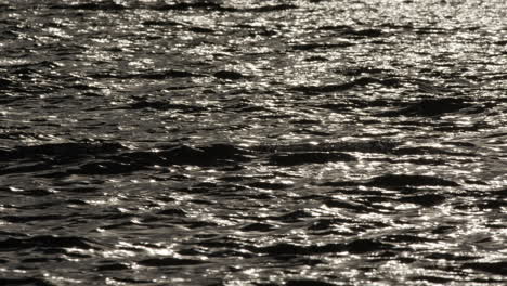 Shimmering-light-across-dark-grey-black-water-with-natural-ripple-wave-surface