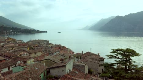 Experience-the-tranquil-charm-of-Malcesine's-cityscape-against-a-backdrop-of-majestic-mountains-and-birds-soaring-at-sunset