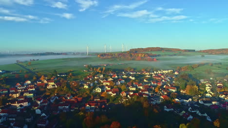 Aerial-view-over-a-european-town-with-wind-tubine-background,-foggy-sunrise