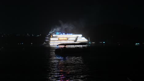 Illuminated-cruise-ship-at-night,-visible-across-dark-waters-with-lights-reflecting-on-surface,-wide-shot