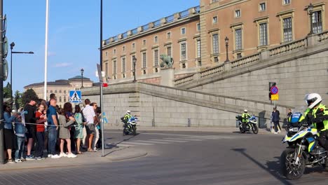 Crowd-awaiting-royal-procession-at-Swedish-Palace-on-National-Day,-police-presence,-sunny-day,-city-landmark