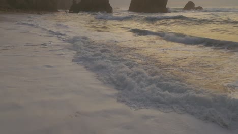 Aerial-view-tilting-over-waves-clos-to-rocky-cliffs-on-Atlantic-Ocean-at-the-Ursa-Beach,-cloudy-sunset-in-Portugal