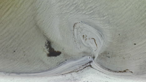 Vista-Aérea-De-Una-Playa-Donde-La-Interacción-De-Arena-Y-Agua-Ha-Creado-Patrones-Intrincados-Y-Arremolinados.