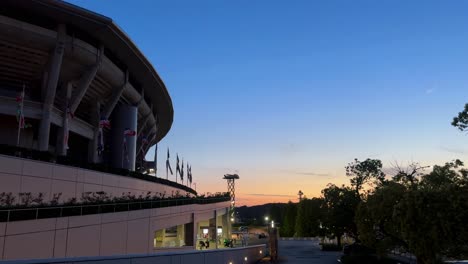 Außenansicht-Des-Stadions-Bei-Sonnenuntergang,-Klarer-Himmel-Und-Wehende-Fahnen,-Eine-Urbane,-Moderne-Architekturkulisse
