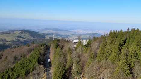 White-camper-van-driving-on-a-mountain-road-with-city-of-Freiburg-im-Breisgau-visible-in-the-far-background