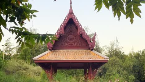 Tracking-shot-of-ornamented-Pagoda-from-Plaza-Thailand-through-hang-tree-branchs,-Araucano-Park