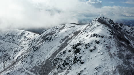 Picos-Montañosos-Cubiertos-De-Nieve-Con-Nubes-Arremolinándose,-Filmados-Durante-El-Día,-Vista-Aérea