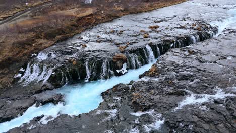 Aerial-shot-of-the-striking-Bruarfoss-waterfall-with-vibrant-blue-waters-in-Iceland,-barren-landscape