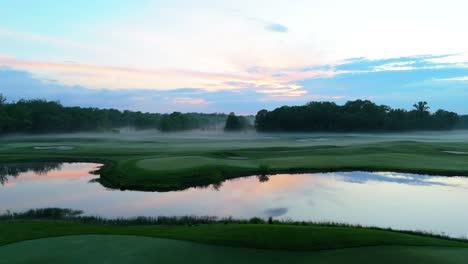 Flyby-on-a-golf-course-with-a-stunning-showcase-of-fog-slowly-creeping-out-of-the-forest-line