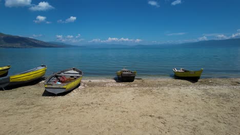 Tranquil-Shore-of-Lake-Ohrid-in-Pogradec:-Clean,-Calm-Waters-and-Serene-Landscape-Under-the-Blue-Sky-with-White-Clouds-on-Empty-Beach