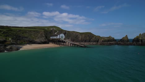 RNLI-Padstow-Lifeboat-Station-at-Trevose-in-Cornwall-with-Low-Aerial-Panning-Arc-Shot-Over-Water-with-Scenic-Views-of-the-Cornish-Coastline,-UK