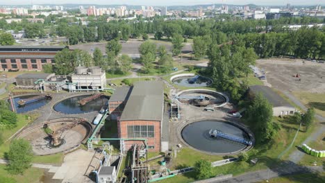 Luftaufnahme-Einer-Kläranlage-Mit-Mehreren-Runden-Tanks-Inmitten-Von-Grünflächen-Und-Städtischen-Strukturen